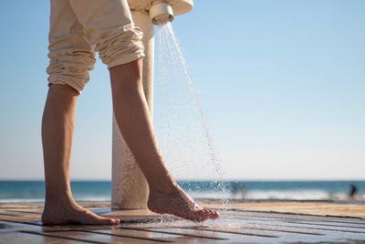 Woman wetting her feet with a shower to clean them from the sand after leaving the beach.