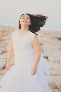 Beautiful young woman at beach against sky