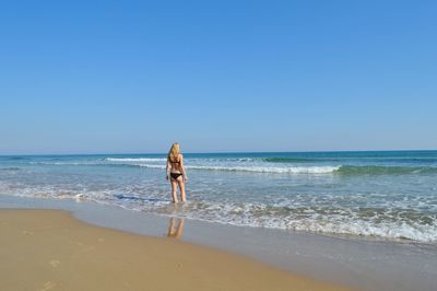 Rear view of woman in bikini standing on beach against clear sky