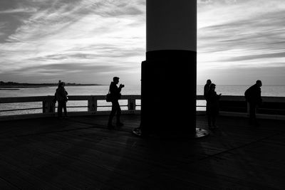 Silhouette people standing by sea against sky