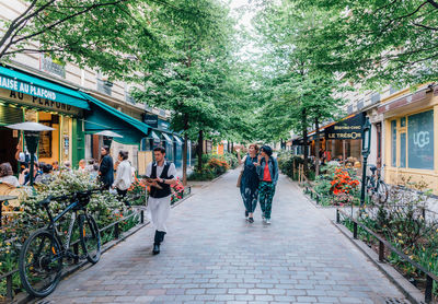 People walking on footpath amidst plants in city