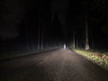 Rear view of man walking on road along trees at night