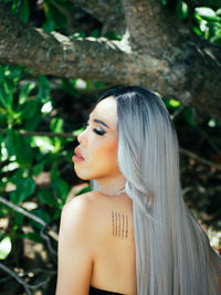 Portrait of young trans woman standing against tree