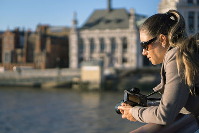 Side view of thoughtful woman with camera leaning on railing against river