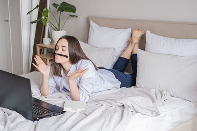 Portrait of young woman using mobile phone while sitting on bed at home