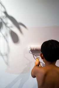 Repair in the apartment. happy child shirtless asian boy paints the wall with pastel pink paint.