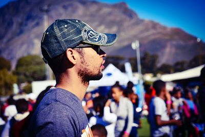 Side view of young man wearing cap against mountain during sunny day