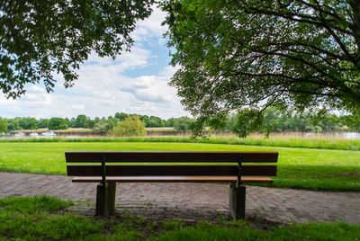 Empty bench in park against sky