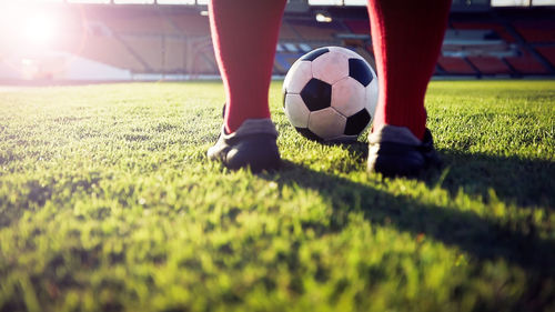 Low section of man playing soccer at stadium on sunny day