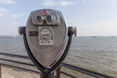 Close-up of coin-operated binoculars by sea against sky