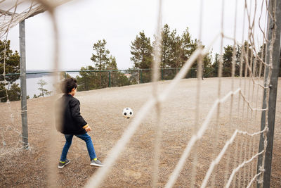 Rear view of boy standing on goal post at school playground