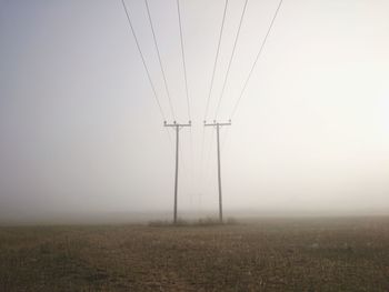 Electricity pylon on field against sky during foggy weather