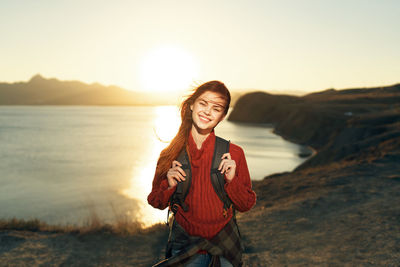 Portrait of smiling young woman standing on land against sky during sunset