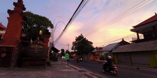 People on street amidst buildings against sky at sunset