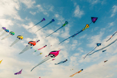 Low angle view of kites flying in cloudy sky