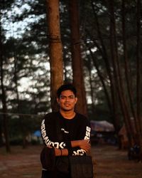 Portrait of young man standing against trees in forest