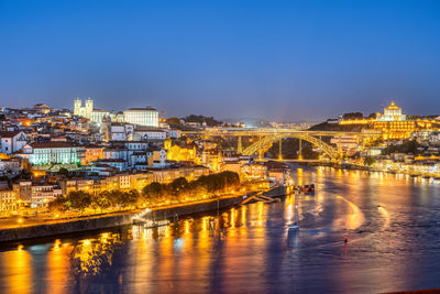 Illuminated buildings by river against sky at night