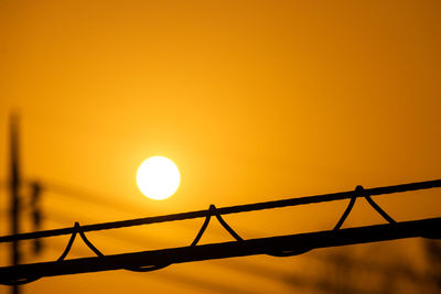 Low angle view of electricity pylon against orange sky