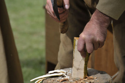 Midsection of carpenter cutting wood on tree stump