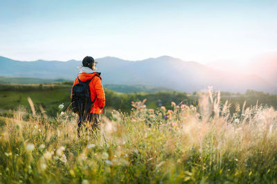 Rear view of man hiking on field against mountain and sky at sunset