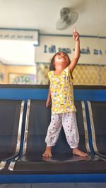 Full length of girl with hand raised standing on chair
