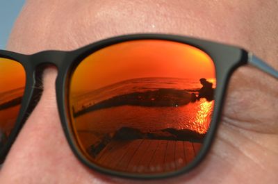 Close-up of reflection of sunglasses on mirror against orange sky