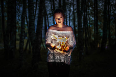 Digital composite image of woman holding fire while standing in forest at night