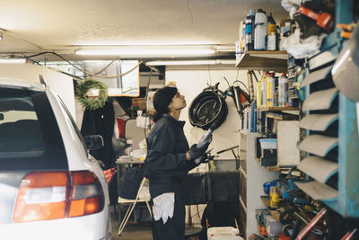 Side view of female mechanic looking at bottles on shelf at auto repair shop