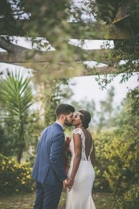 Bride and groom kissing against plants at park