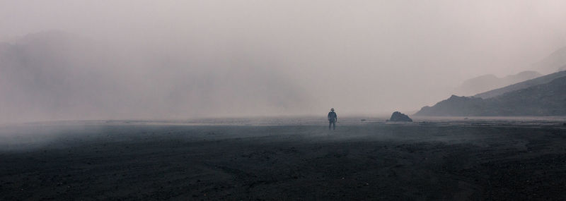 Man walking on landscape against sky during foggy weather