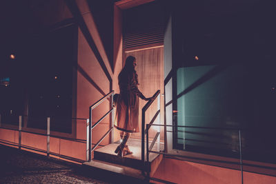 Rear view of woman walking towards entrance at night