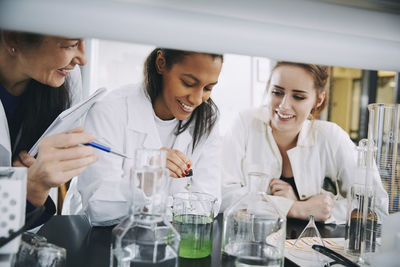 Smiling multi-ethnic university students with mature teacher mixing solution in laboratory