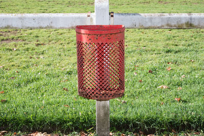 Close-up of red garbage bin on railing at park