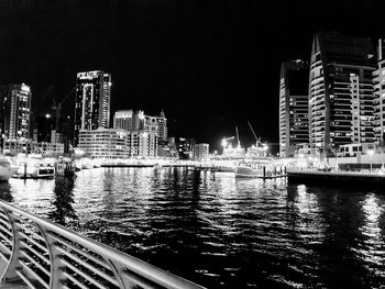 River by illuminated buildings against sky at night