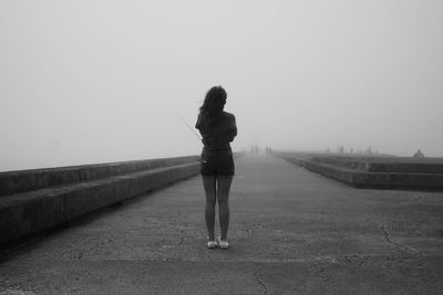 Rear view of woman standing on walkway against sky