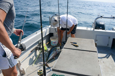 People catching fish while standing in boat on sea