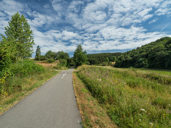 Empty road amidst field against sky