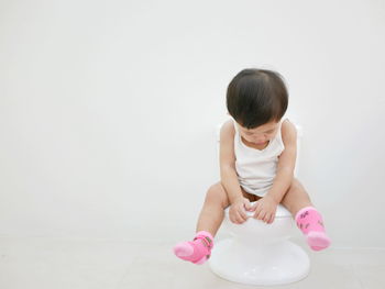 Cute girl sitting on toilet bowl against white background