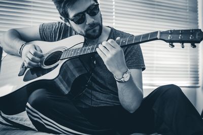 Man playing guitar while sitting on bed at home