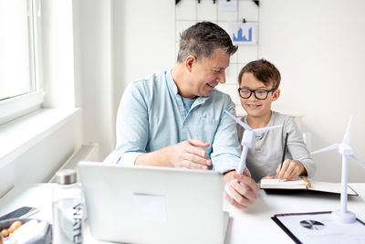 Father and son with toy and laptop on table at home