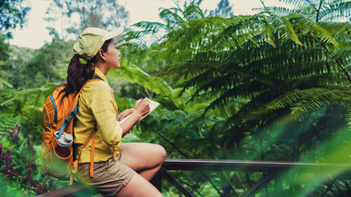 Young woman sitting on plant against trees
