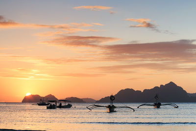 Boats in sea by mountains against cloudy sky during sunset
