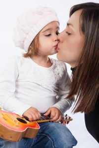 Mother kissing daughter with ukulele against white background