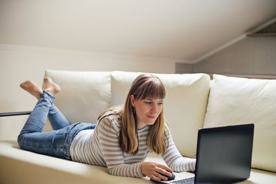 Woman using laptop while lying on sofa at home