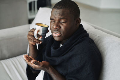 Full length of man drinking coffee while sitting on sofa