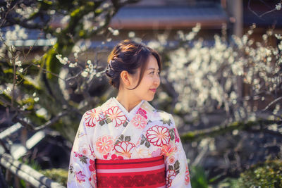 Smiling beautiful woman in traditional cloths standing against cherry trees