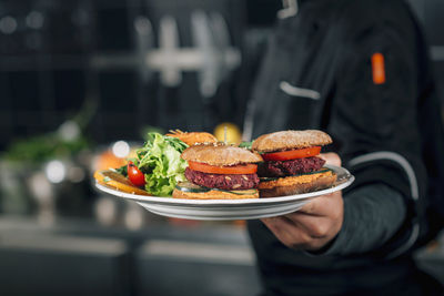 Midsection of chef holding burgers in plates at restaurant