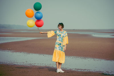 Full length of young woman holding colorful balloons at beach