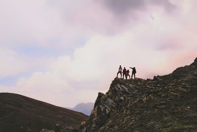 Low angle view of hikers standing on cliff against cloudy sky