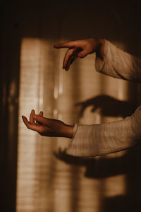 Cropped image of woman hand against curtain in dark room